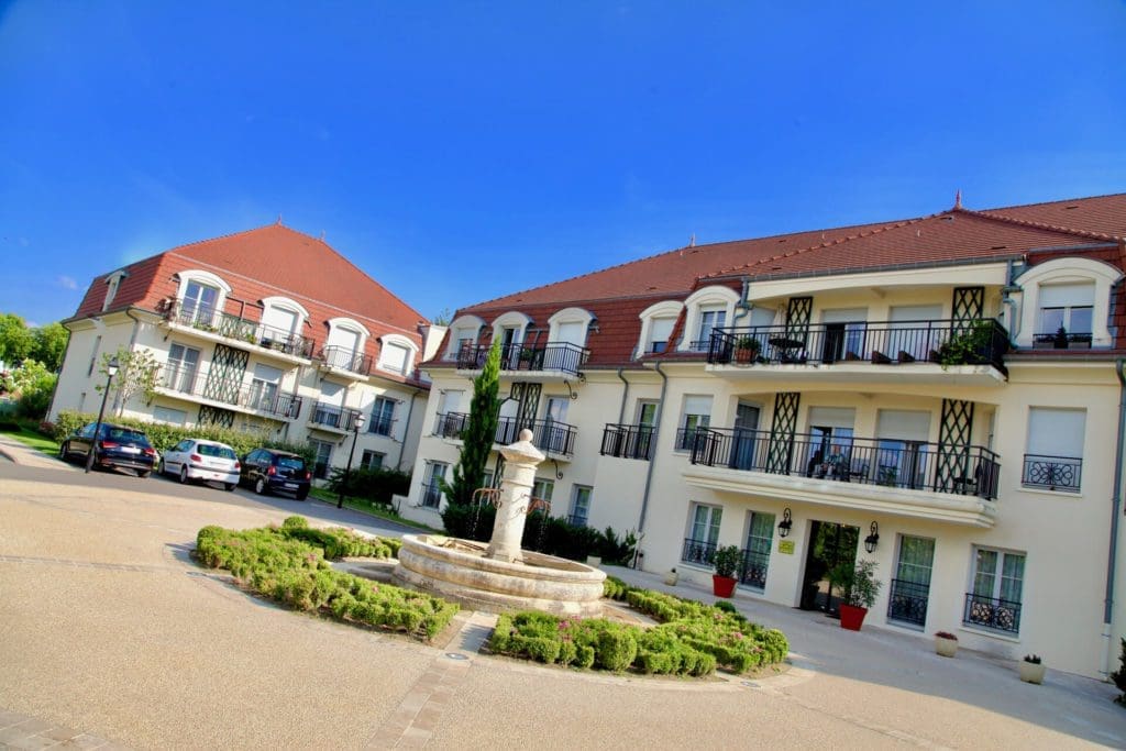Parking et vue extérieure Résidences senior Beaune avec fontaine en place centrale